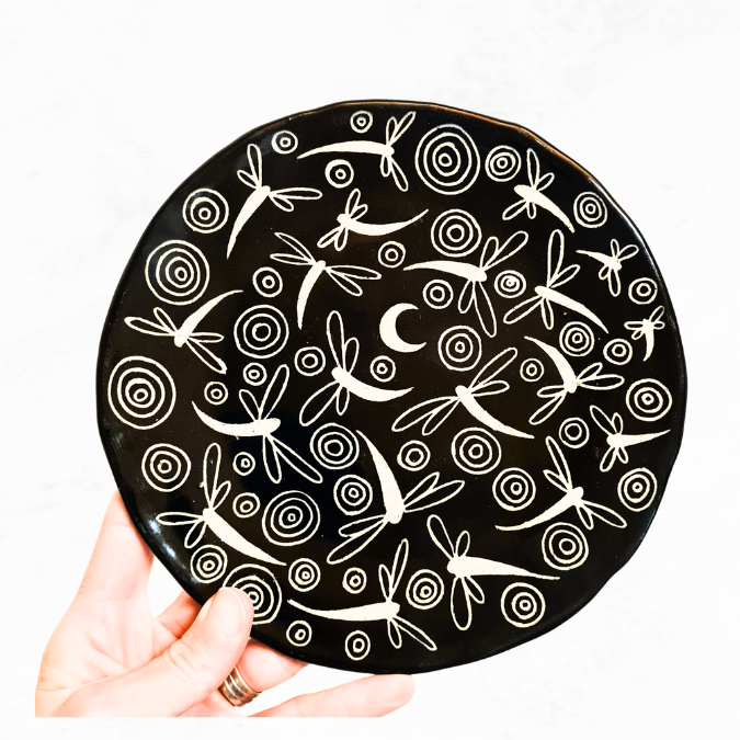 Ceramic plate decorated with crescent moon, numerous dragonflies and circle ripples, black and white in colour.