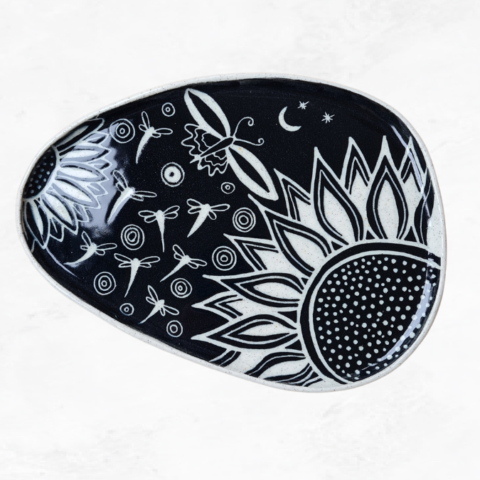 Ceramic plate, decorated with two half flowers, dragonflies, butterflies, and circle ripples, black and white in colour.