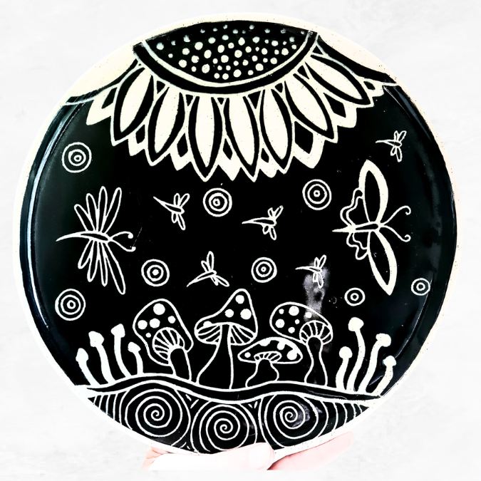 Ceramic large plate, decorated with half a large flower, mushrooms, dragonflies, butterflies, and circle ripples, black and white in colour.